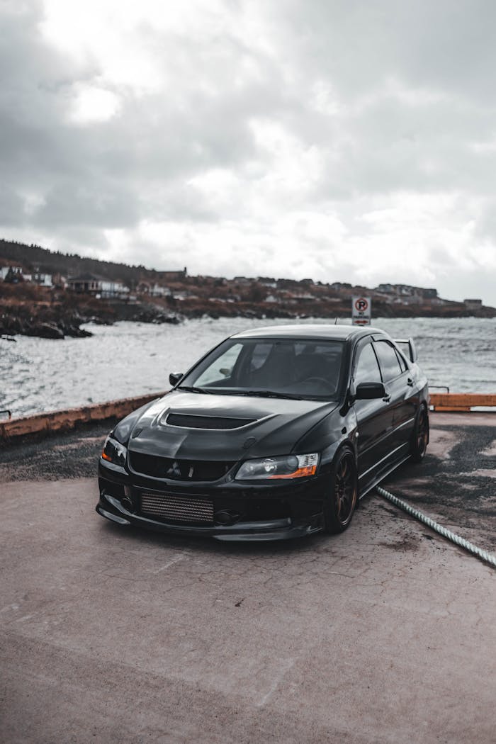 Black car parked on a waterfront, capturing a blend of modern automotive design and natural beauty.